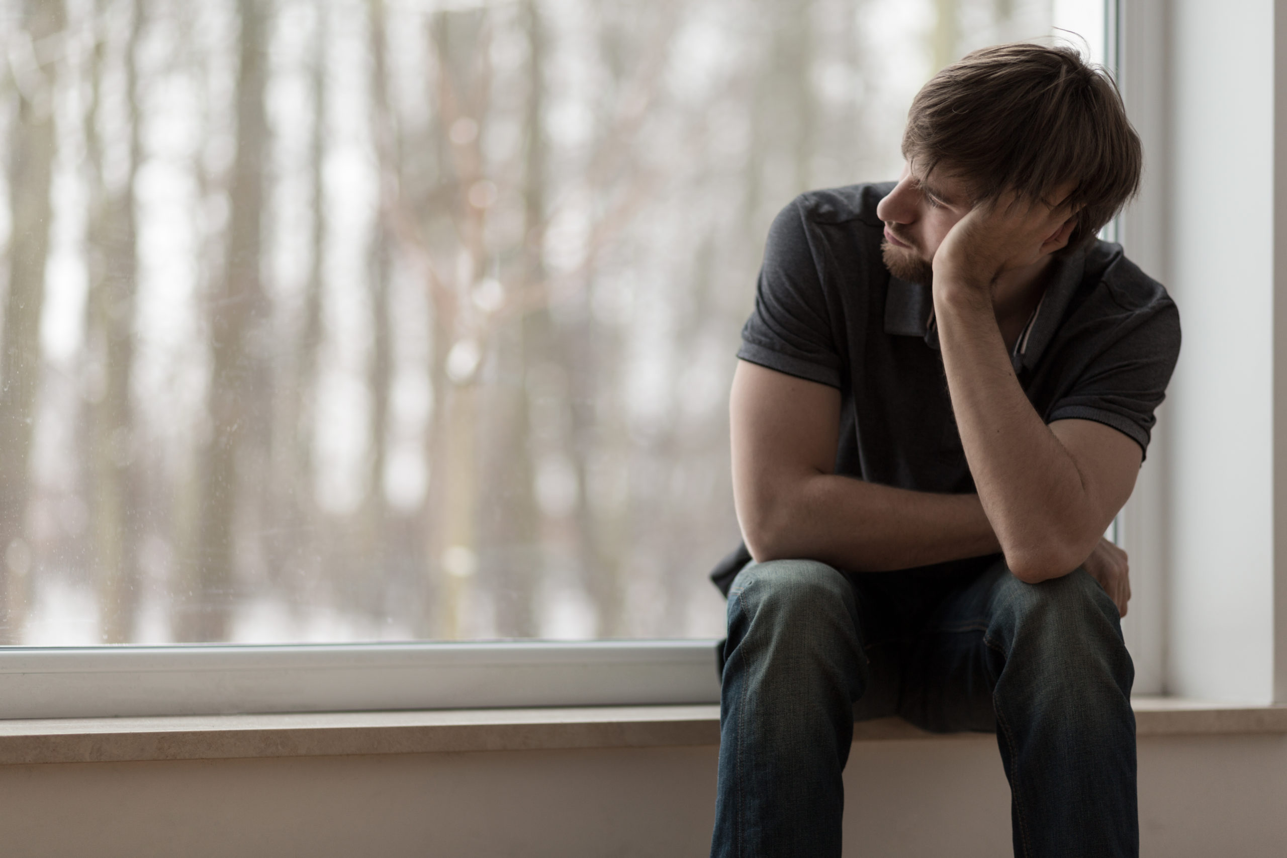 Man sitting on a window ledge with his elbow propped on his knee, his head leaning on his hand. 